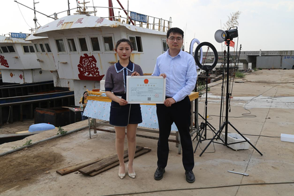 海鮮電商張夢(mèng)琴與幫辦員手持食品經(jīng)營許可證合影。贛榆區(qū)委宣傳部供圖