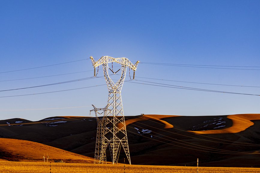 阿里地區(qū)的曠野上，電力鐵塔在夕陽下熠熠生輝。